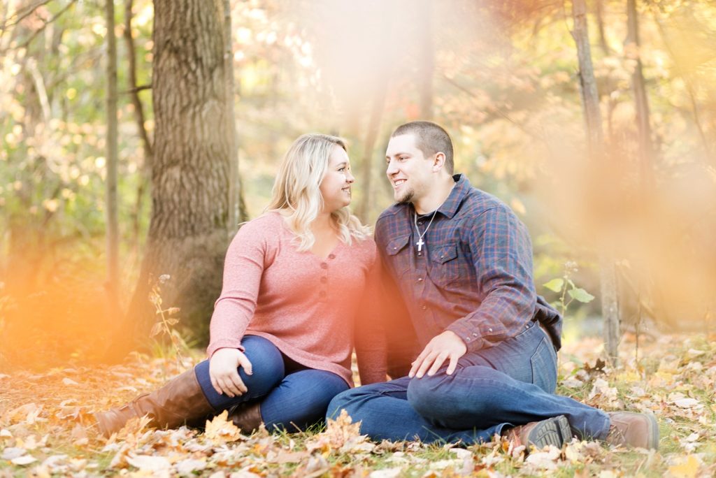 couple sitting in the falling leaves looking at each other at Erickson Park in Chippewa Falls for their engagement session
