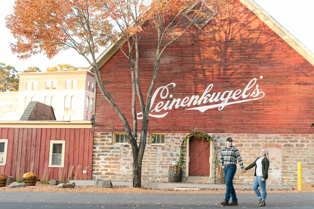 couple walking by the barn at Leinenkugels Brewery in Chippewa Falls for their engagement photos