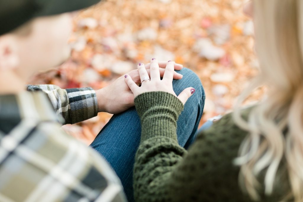 couples hands with leaves in the background showing off her engagement ring at Leinenkugels Brewery in Chippewa Falls for their engagement photos