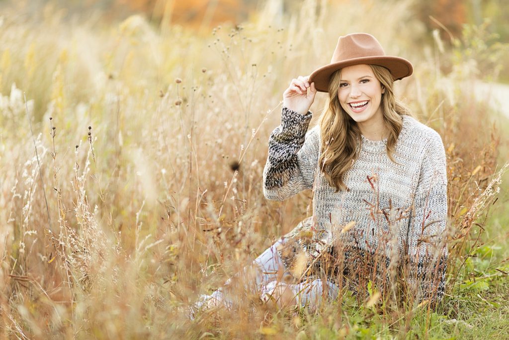 girl sitting in a field for her fall Eau Claire senior photos at River Prairie