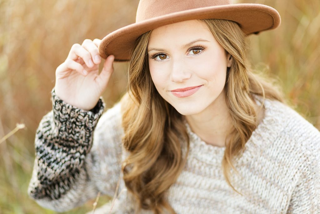girl in a field with a brown hat on smiling for her fall Eau Claire senior photos at River Prairie