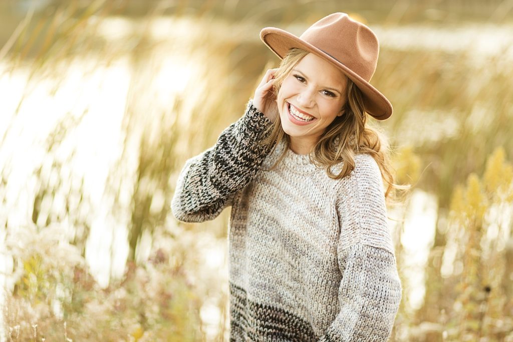 girl standing in tall grass by the water for her fall Eau Claire senior photos at River Prairie