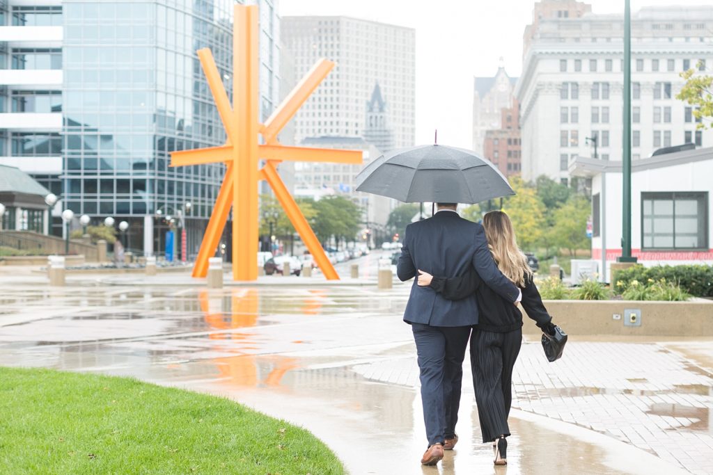 couple walking away towards downtown Milwaukee after he proposes in the rain at the Milwaukee Art Museum