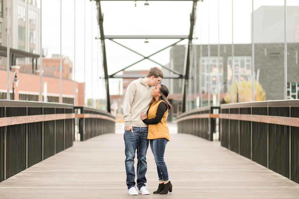 couple on the bridge in Phoenix Park with the Pablo Center behind them in Eau Claire for their engagement photos