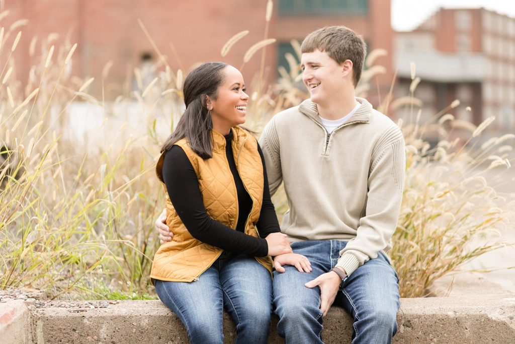couple laughing together sitting on concrete at Banbury Place in Eau Claire for their engagement photos