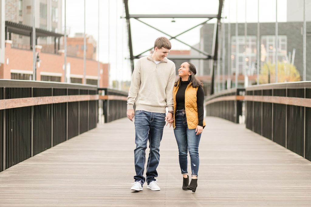 couple walking on bridge with Pablo Center in the background in Eau Claire for their engagement photos