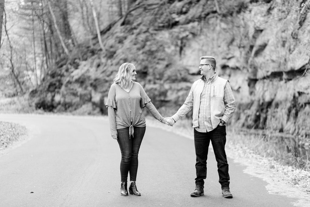 couple in a black and white photo walking down a road for their late fall Irvine Park engagement photos in Chippewa Falls