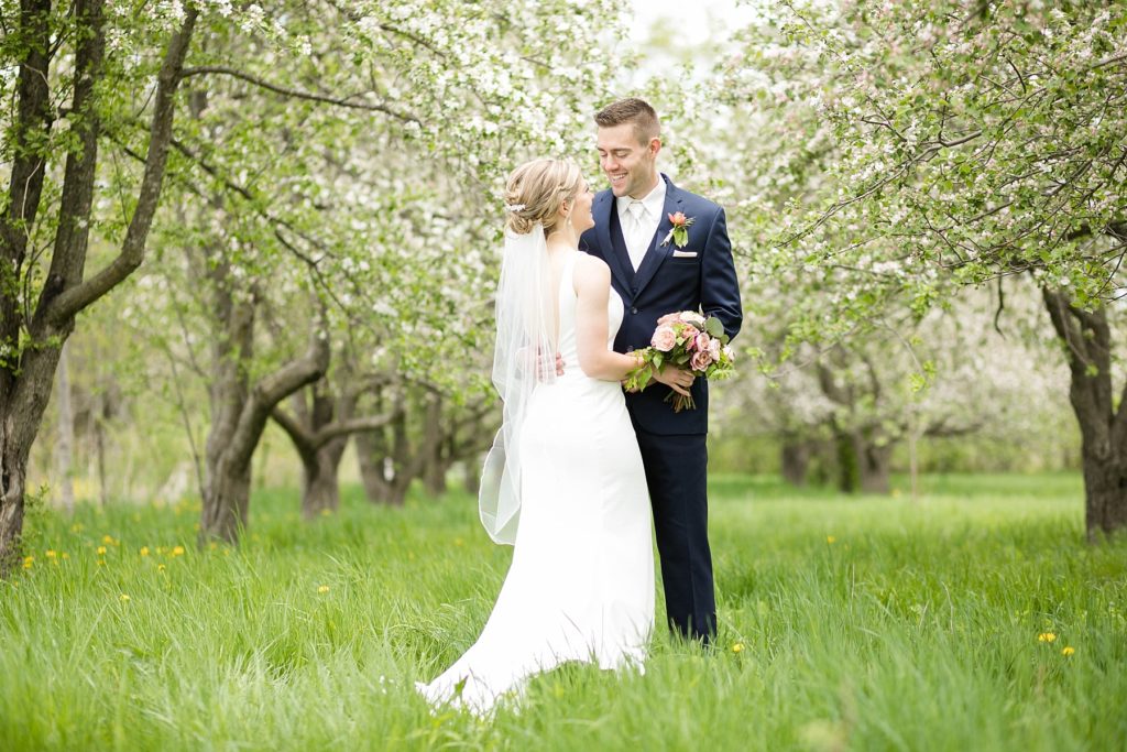 couple in blossomed apple trees for their wedding in Rice Lake, WI at St. Joseph Catholic church and Turtleback Golf