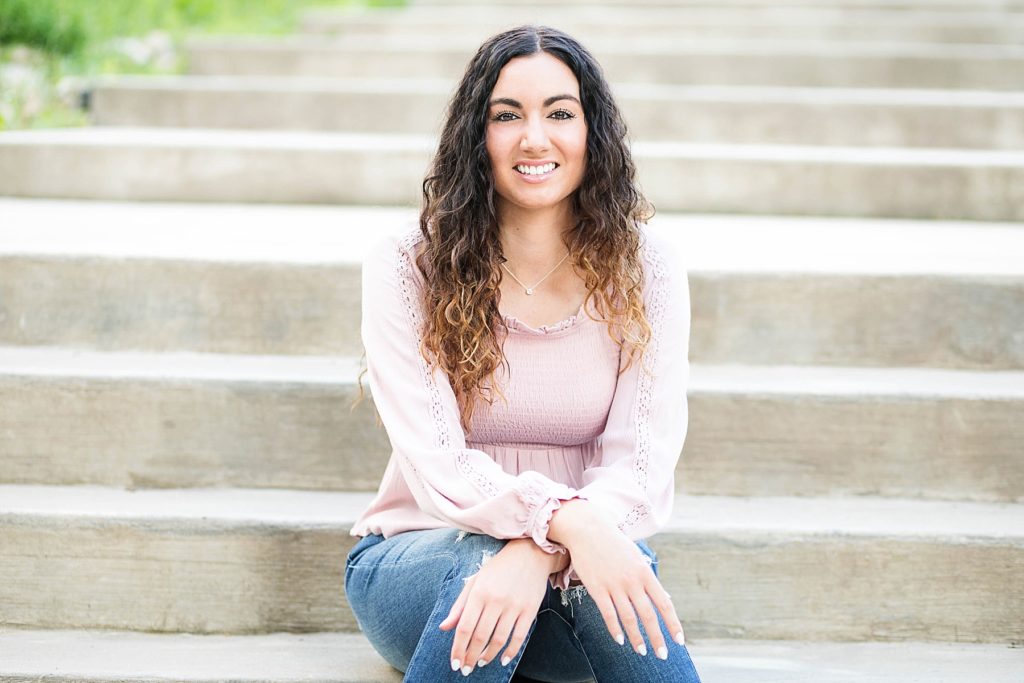 girl in a pink top and jeans sitting on some concrete stairs  for her Eau Claire senior photos