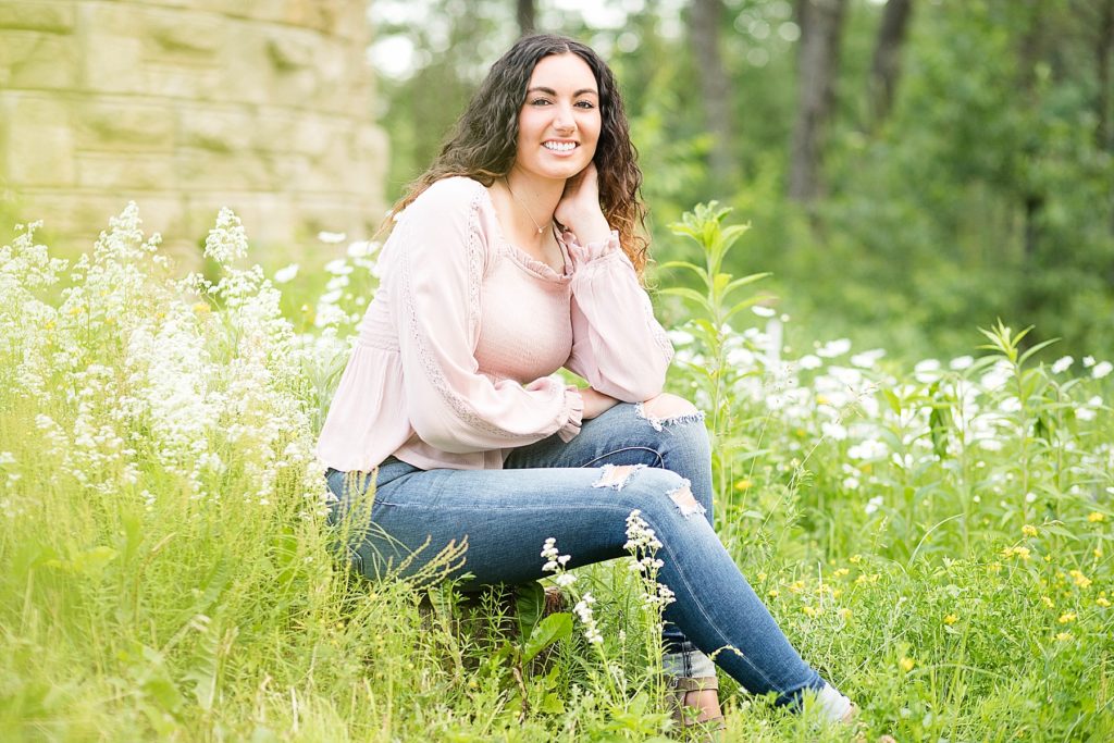 girl sitting in wildflowers in a pink top and ripped jeans for her Eau Claire senior photos