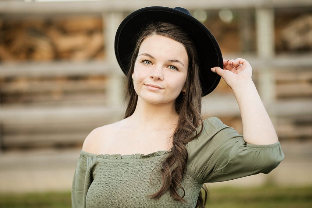 girl at a farm with a black hat on for her boho senior session in Eau Claire, WI