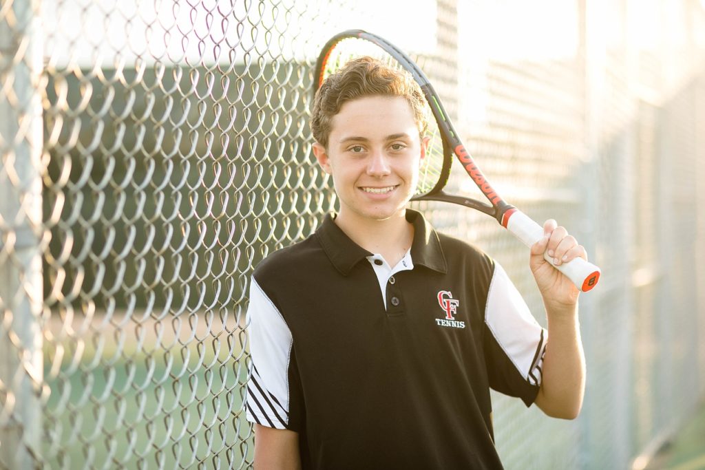 boy with a chippewa falls high school tennis polo on holding his tennis racquet at chi hi on the tennis court for his senior photos