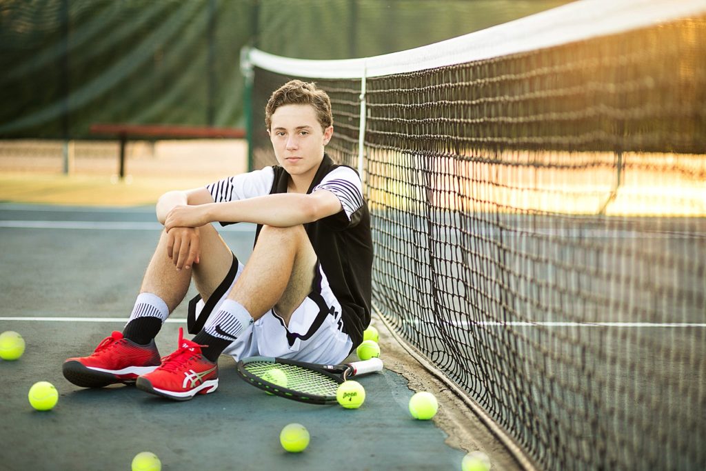 boy leaning against the net at the tennis court at chi-hi in Chippewa Falls for his senior photos