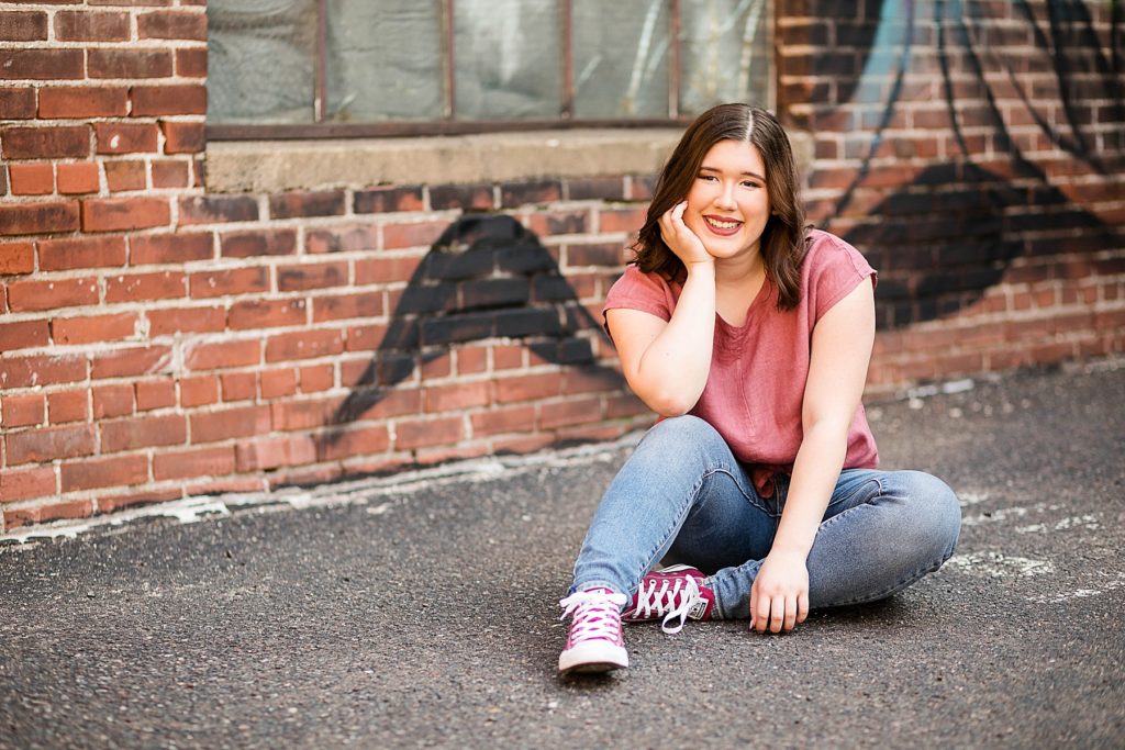 Girl sitting in front of graffiti on a brick wall in Eau Claire for her laid back senior photos