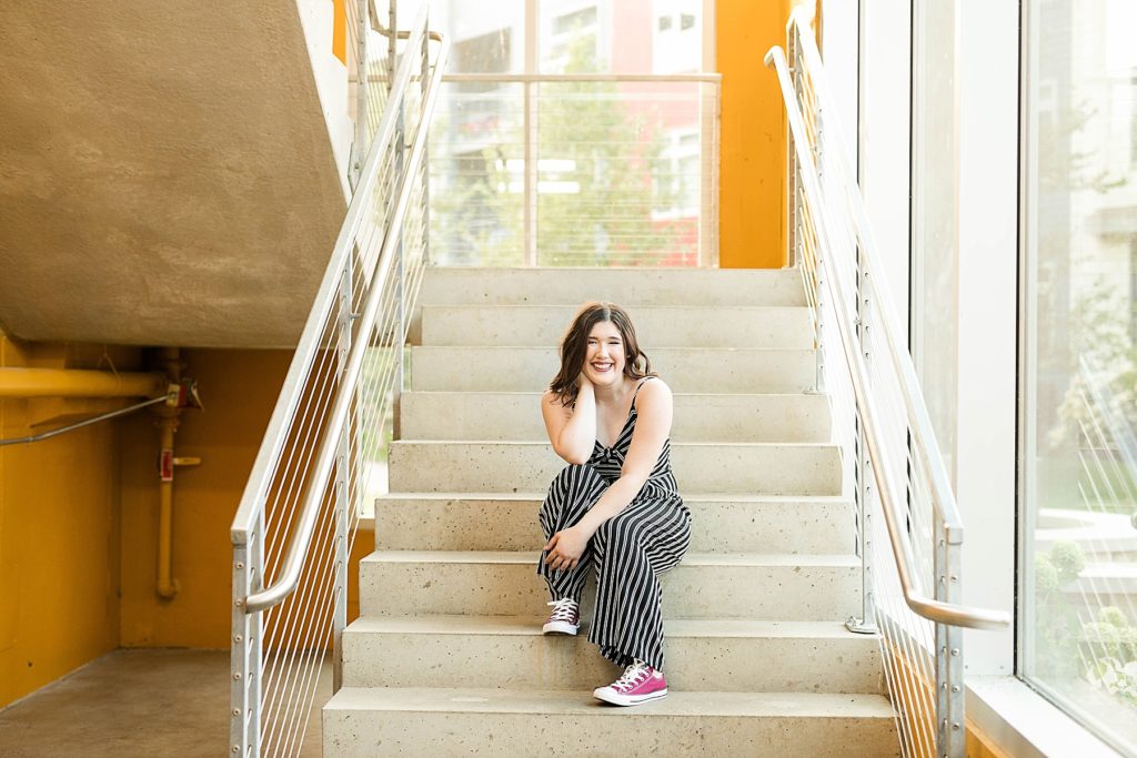 girl sitting on concrete stairs with yellow walls in Eau Claire for her laid back senior photos