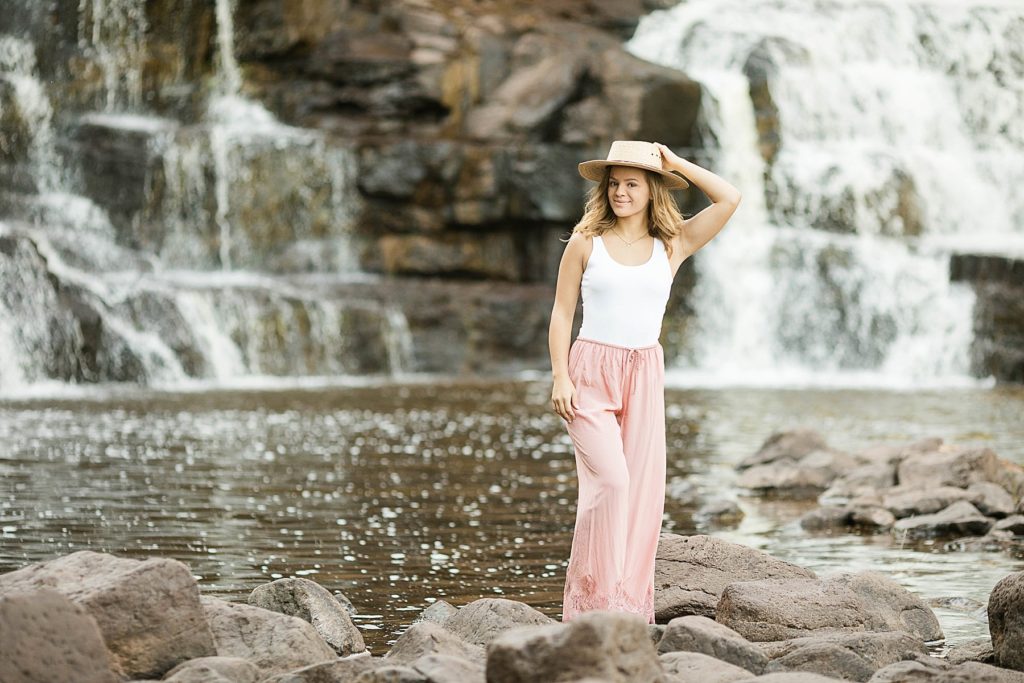 girl standing in rocks below Gooseberry Falls for her North Shore senior photos on Lake Superior