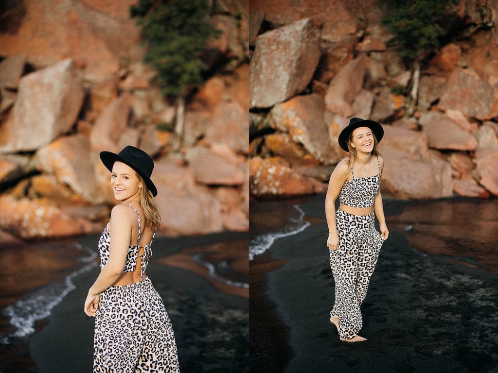 girl stands on a black sand beach on Lake Superior with a black hat on for her North Shore senior pictures