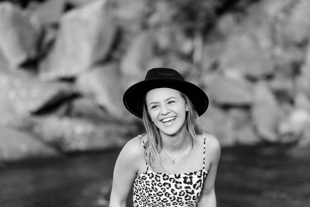 girl laughing in a black and white photo with a black hat on Black Sand Beach in Silver Bay, MN for her senior photos