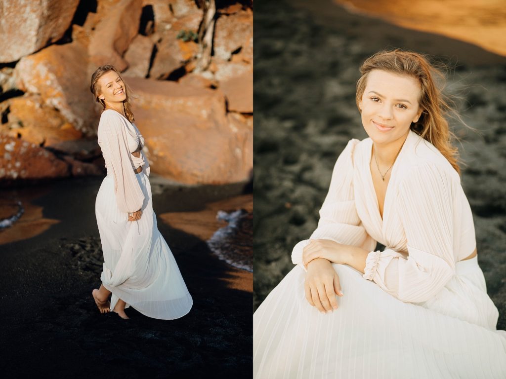 girl sits in on a black sand beach on Lake Superior with a blowing dress on for her North Shore senior pictures