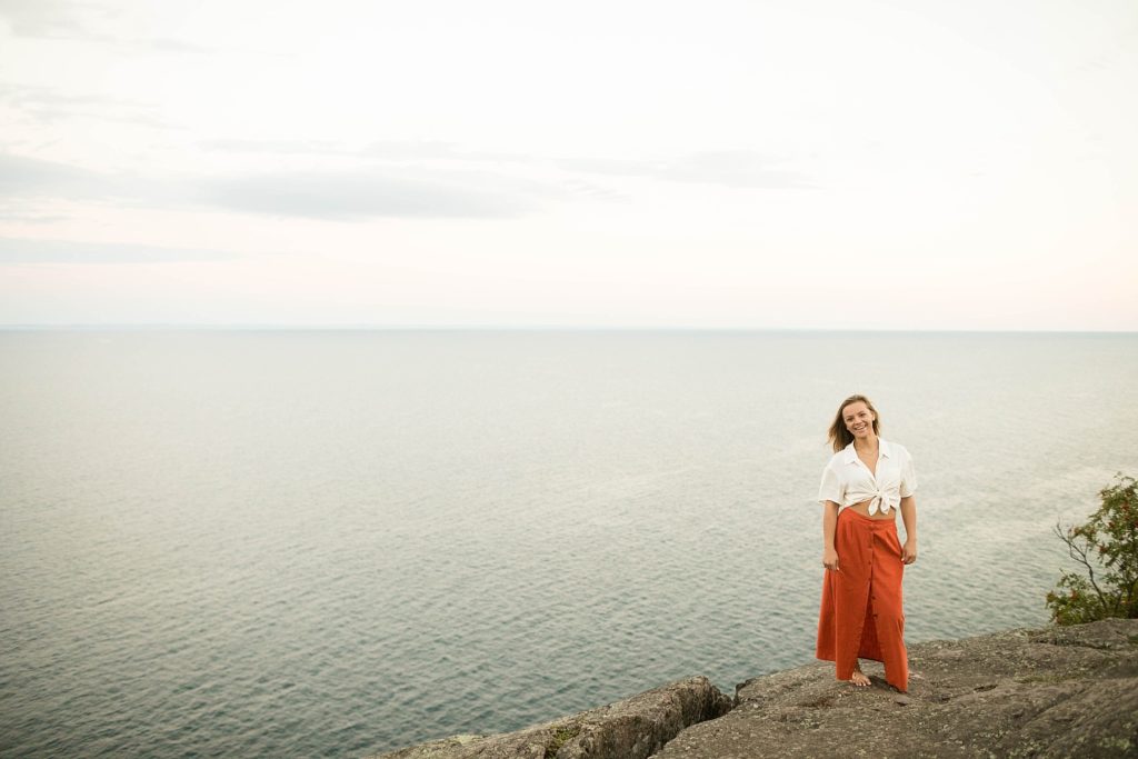 girl standing on rocks at Palisade head in an orange skirt and crop top for her boho senior photos on Lake Superior
