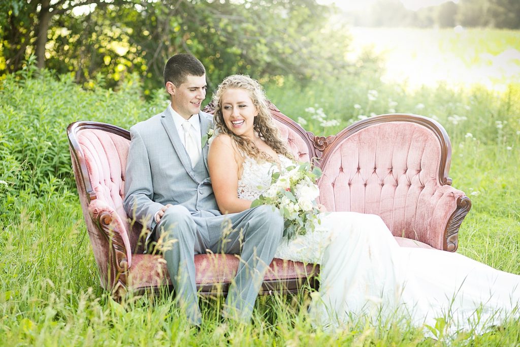 couple sitting on a vintage couch rented from Sweet Legacy in Eau Claire at their summer wedding at the Florian Gardens