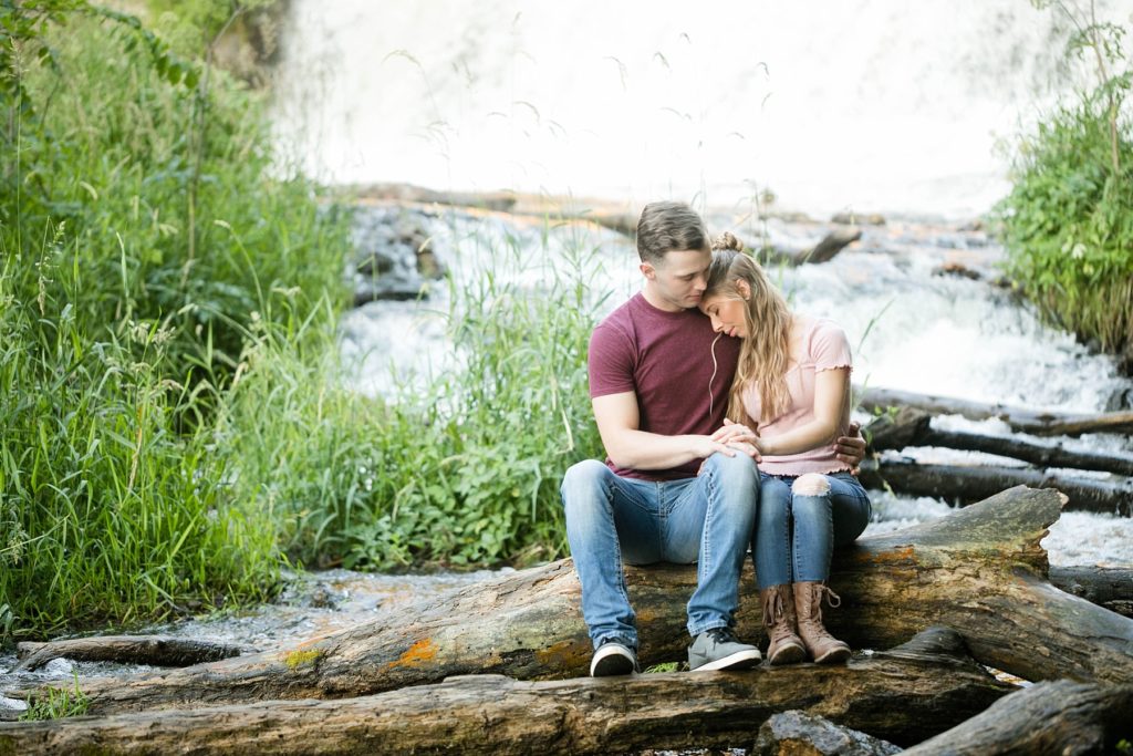 couple sitting in front of the waterfall at Willow River State Park in Hudson, WI for their engagement session