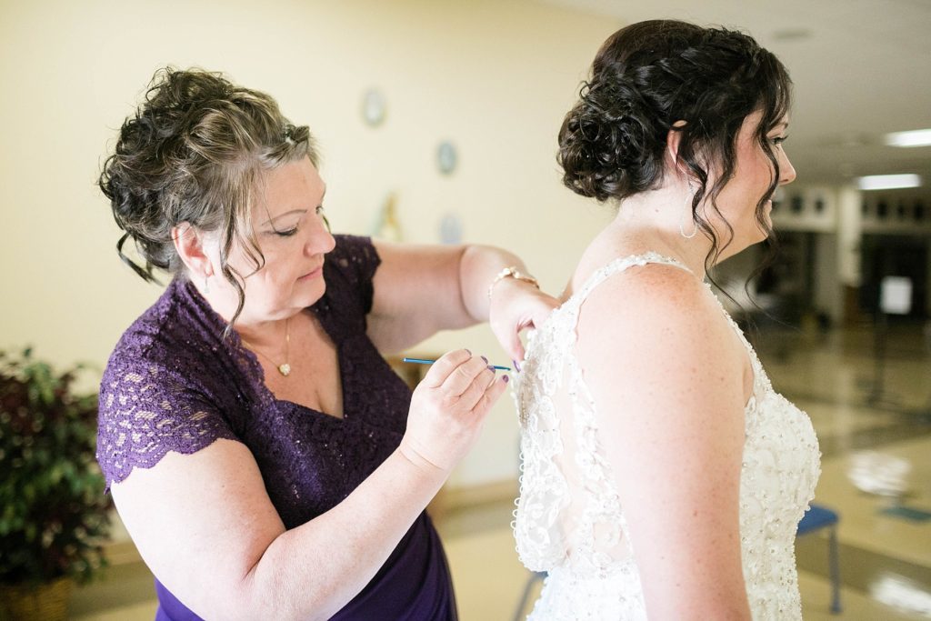 brides mom buttoning the back of her gown before the ceremony at Immaculate Conception Church in Eau Claire