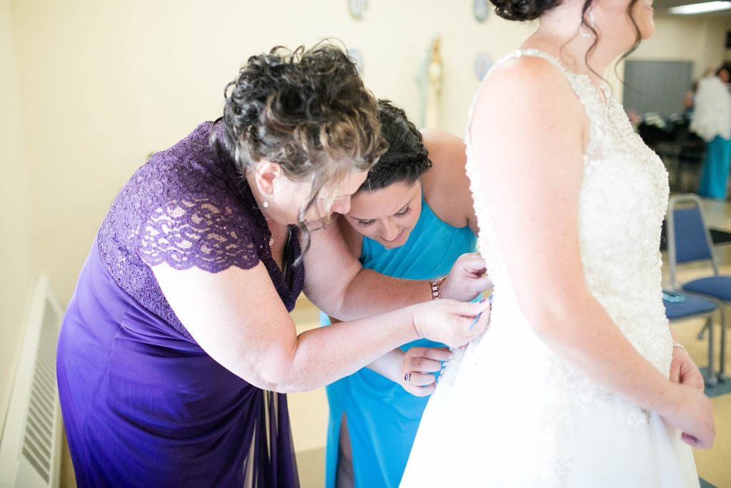 brides mom and sister buttoning her gown at Immaculate Conception Church in Eau Claire