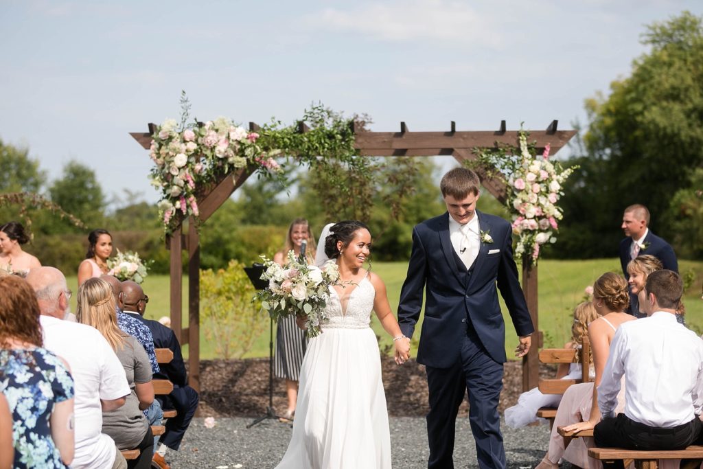 couple walking out of outdoor ceremony with arch behind them and floral at Lilydale in Chippewa Falls, WI