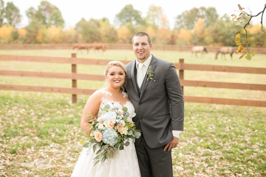 couple smile at the camera on their wedding day with horses in the pasture at their fall wedding at Lilydale in Chippewa Falls