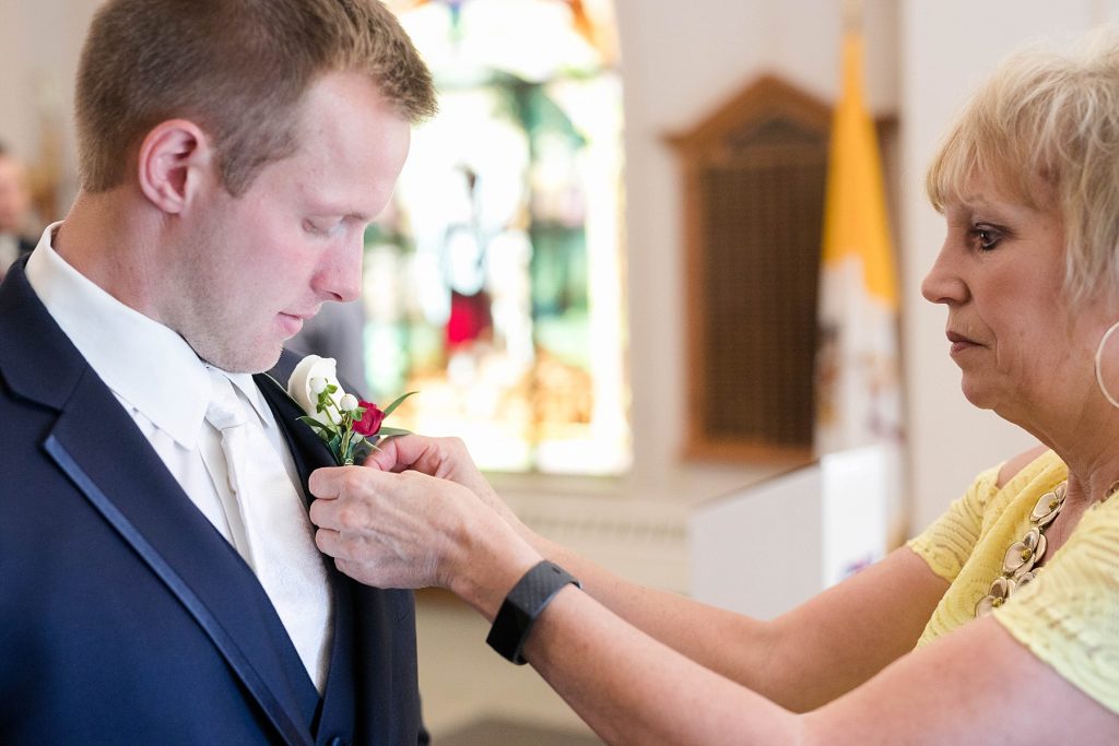 groom getting his flowers pinned on before the wedding ceremony at St. Charles Borromeo Catholic Church in Chippewa Falls