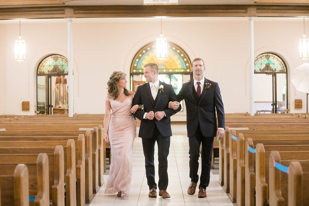 groom being walked down the aisle by both of his parents for an intimate wedding ceremony at St. Charles Borromeo Catholic Church in Chippewa Falls
