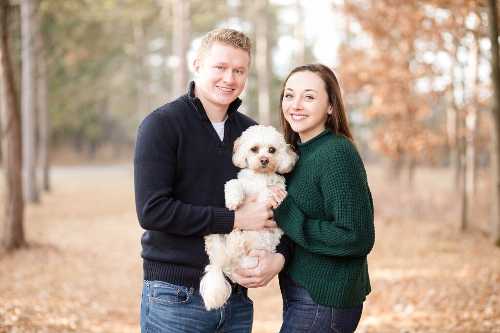 couple holding their dog standing outside in the leaves during the fall for an Eau Claire couple session with dog