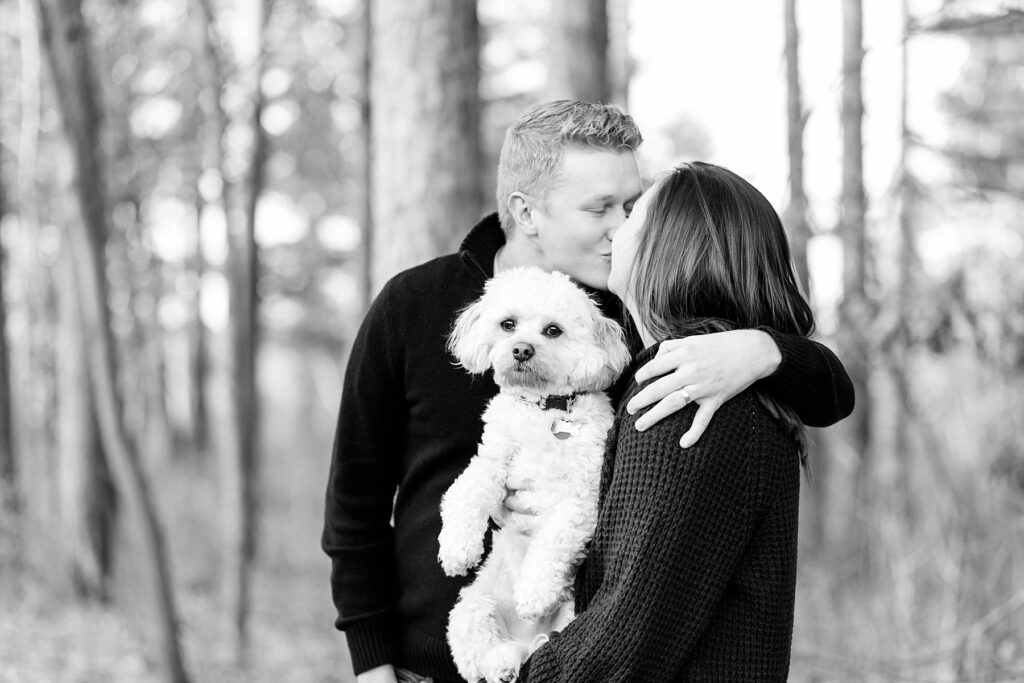 couple kissing in a black and white photo holding their dog for an Eau Claire couple session with dog