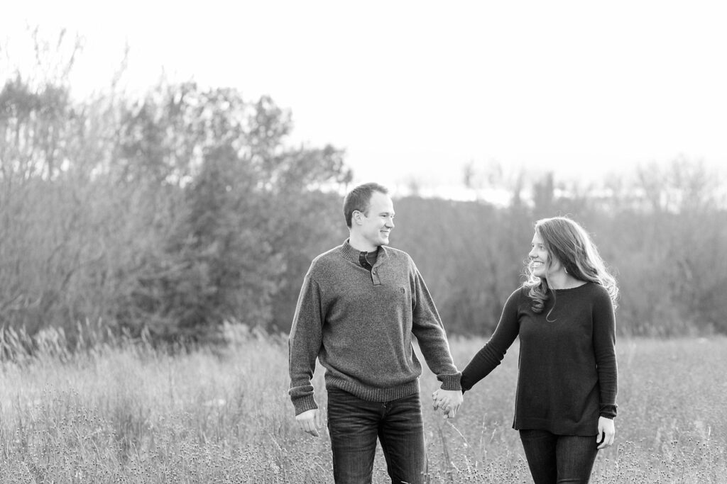 couple walking hand in hand in a black and white photo in a field for their Eau Claire couples session with new puppy
