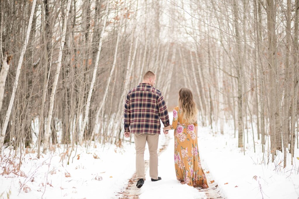 couple walking on a trail through birch trees with snow on the ground for their winter engagement session in Ladysmith